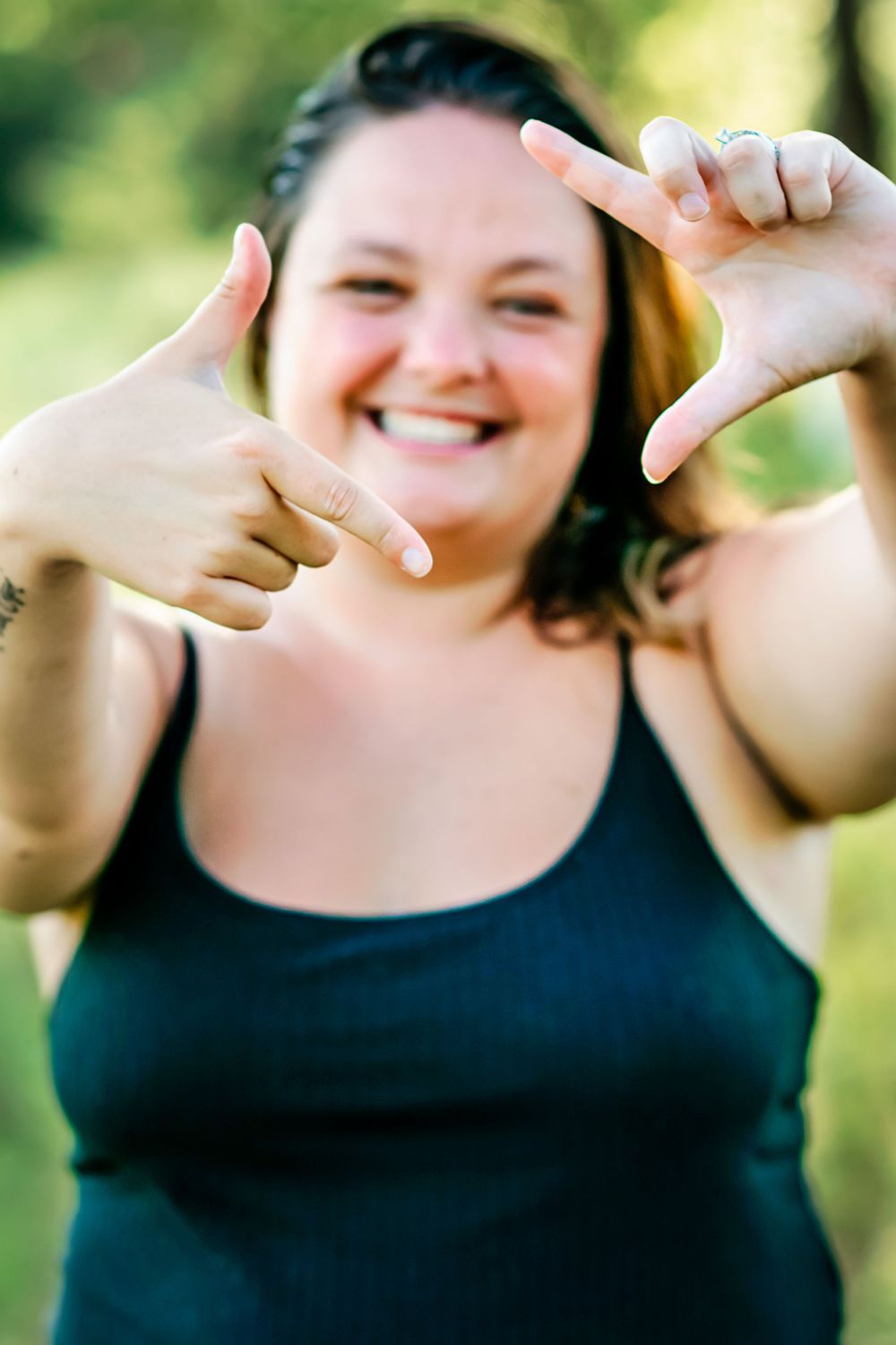 Cheerful person making framing gesture with hands while wearing black tank top outdoors.