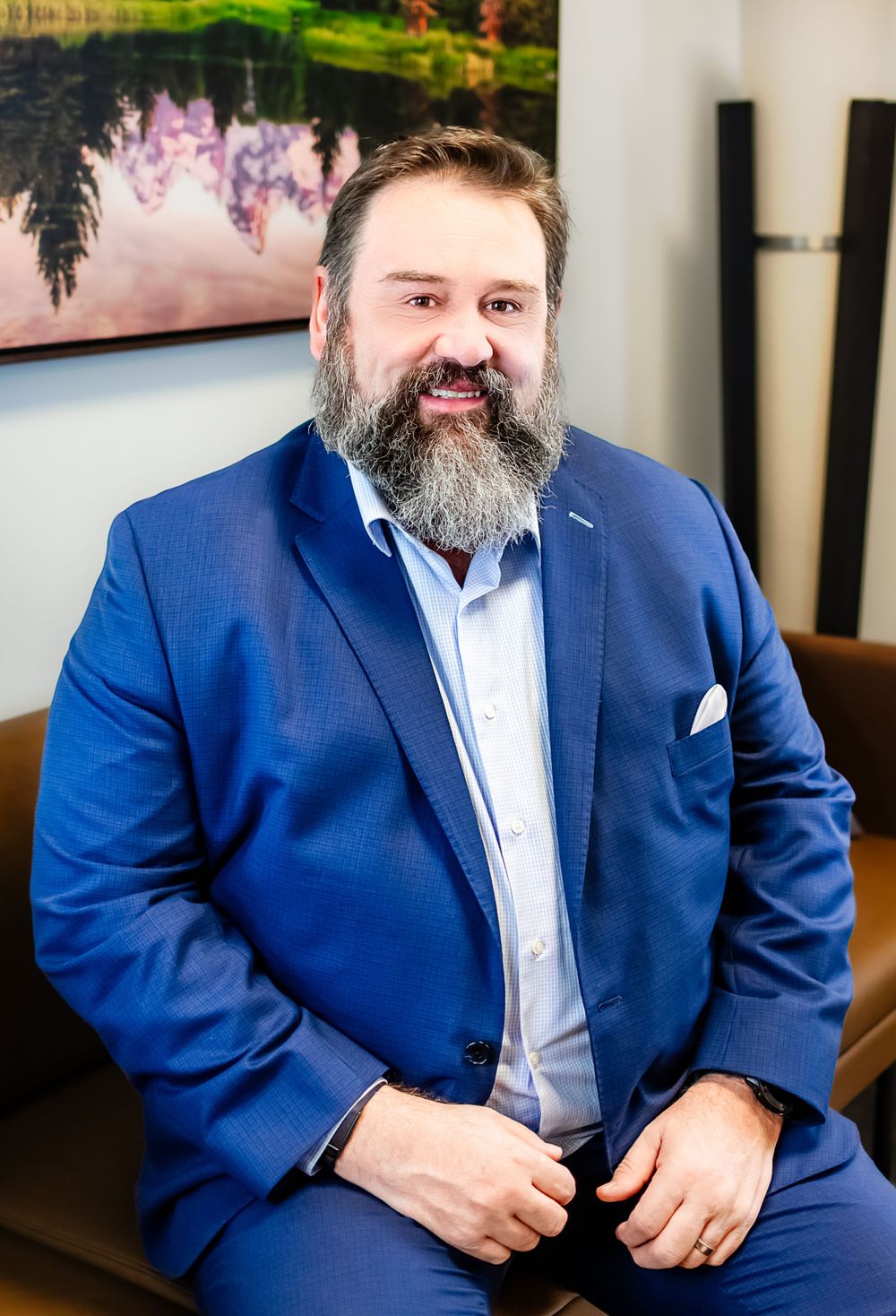 Portrait of bearded professional in navy suit against nature artwork.