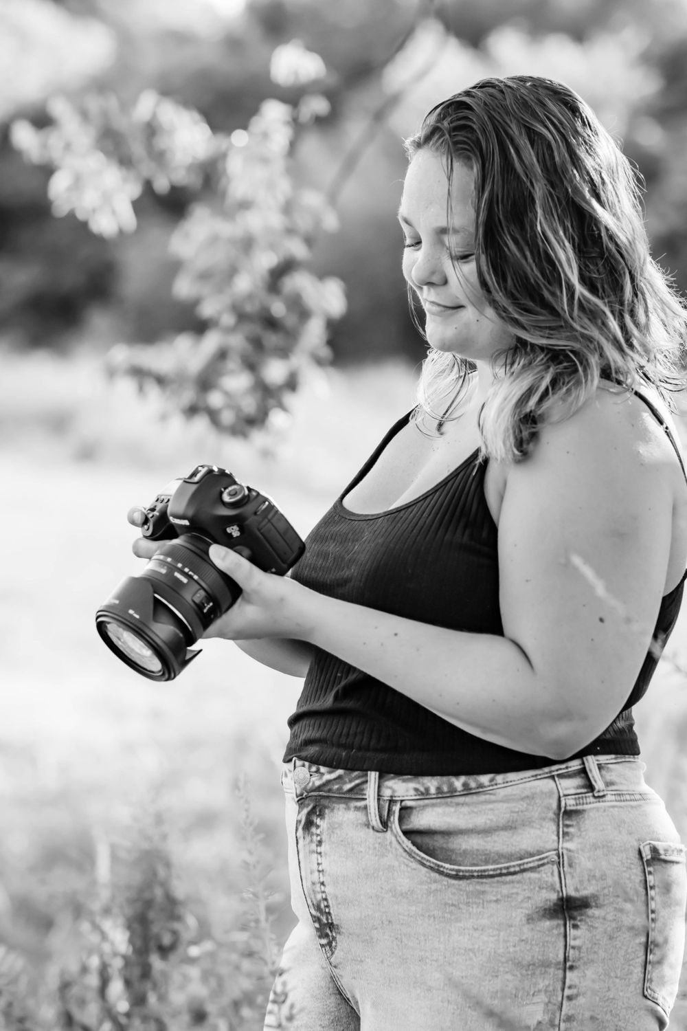 Black and white portrait of photographer reviewing images on camera display in natural setting.