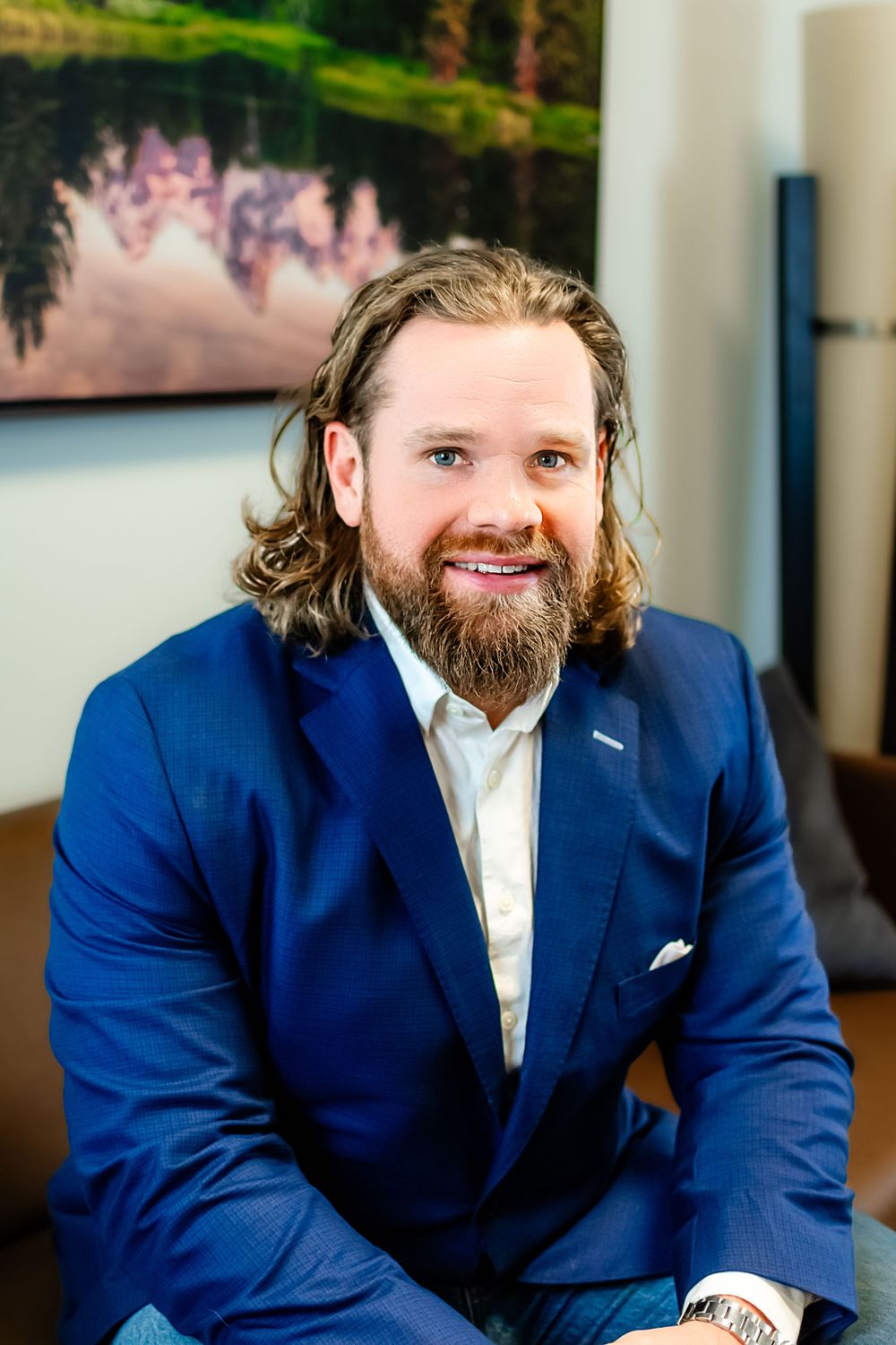 Professional headshot of businessman in blue suit with long beard and hair.