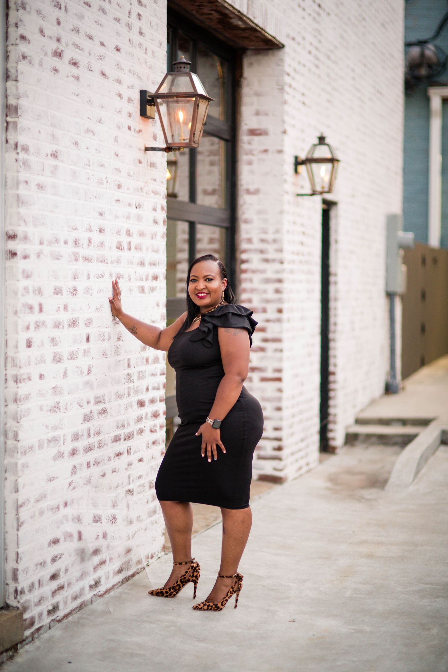 Fashion photo series against white brick wall featuring stylish black dress and high heels.