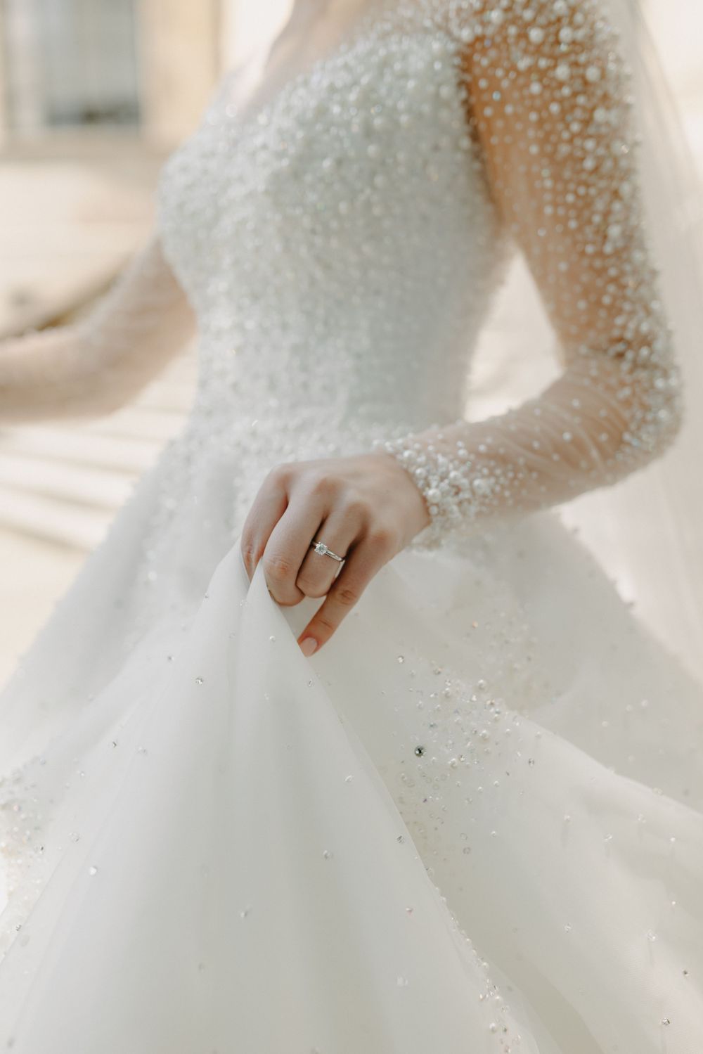 Close-up detail of a sparkling beaded wedding gown and engagement ring.