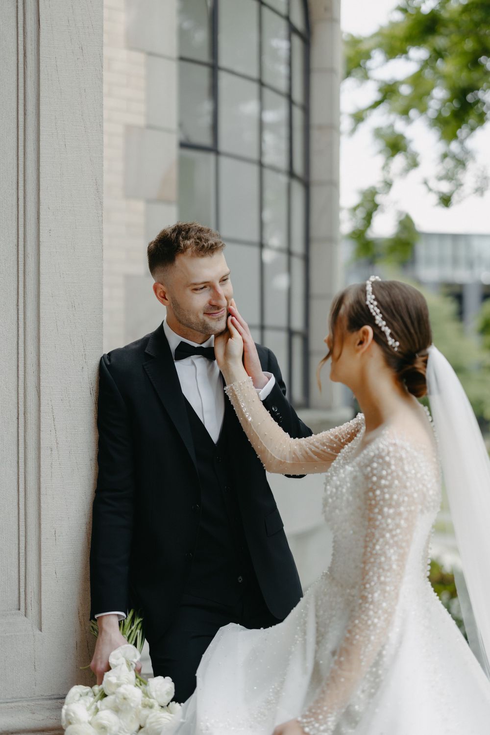 Sweet candid moment between newlyweds as bride touches groom's face near classical architecture.