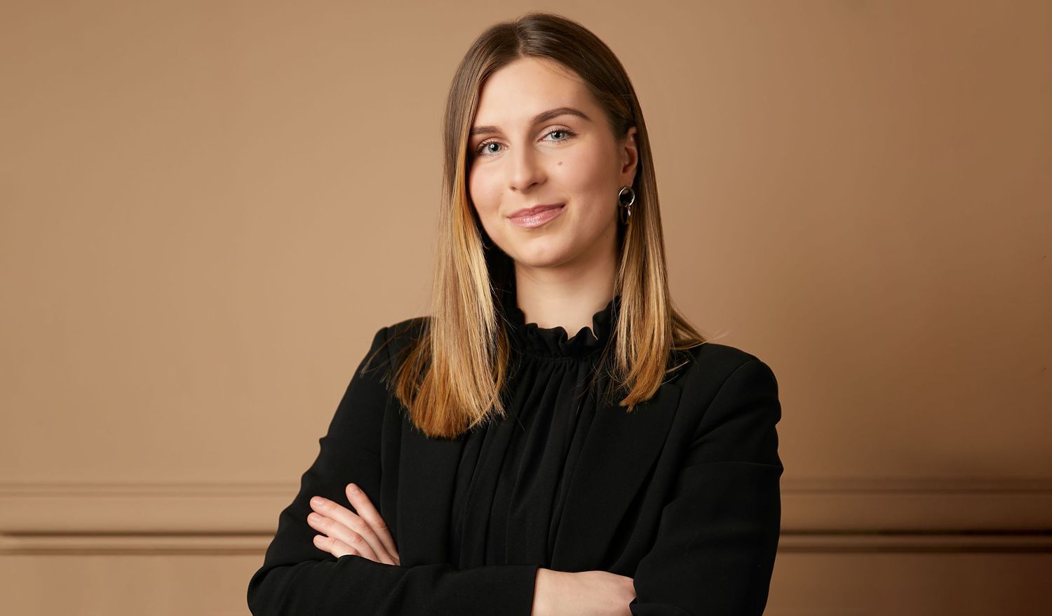 Professional portrait of someone in a black top with arms crossed against a neutral brown background.