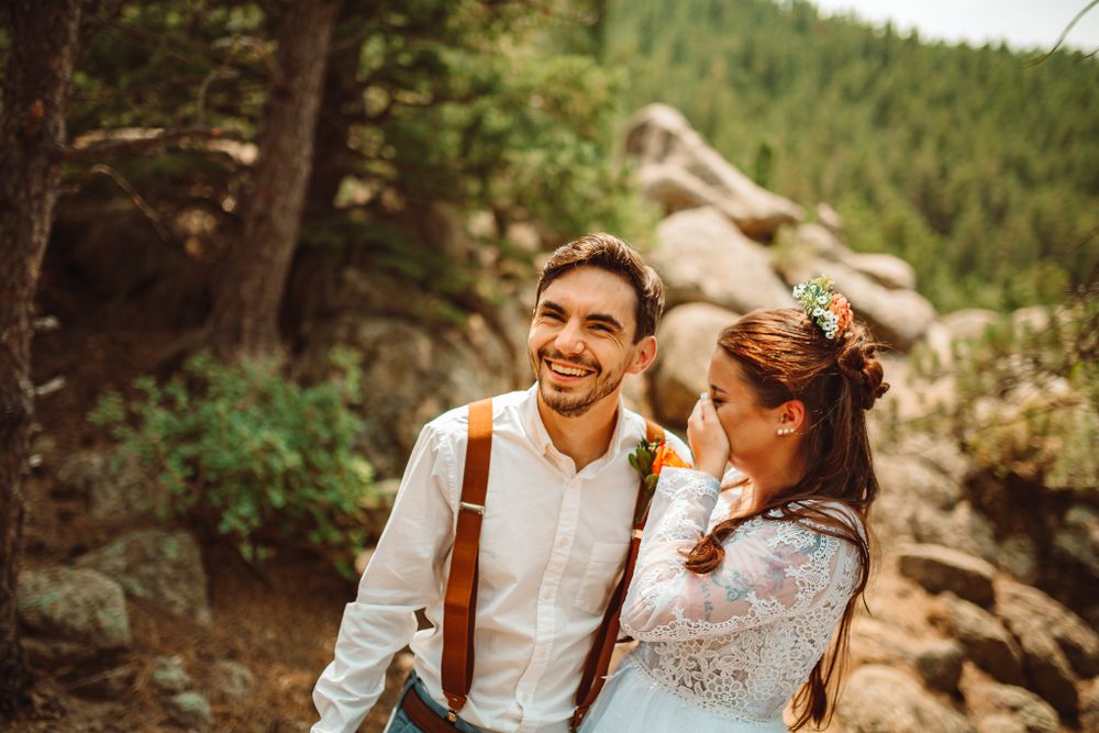 Joyful wedding couple shares a laugh in rocky mountain setting.