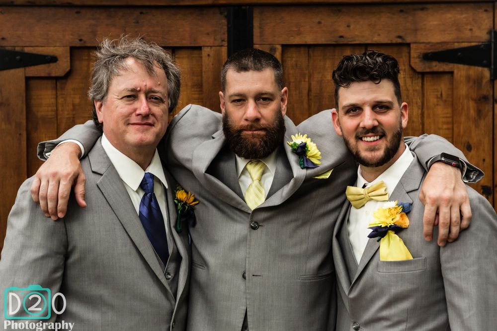 Three groomsmen in gray suits pose together at rustic wooden wall.