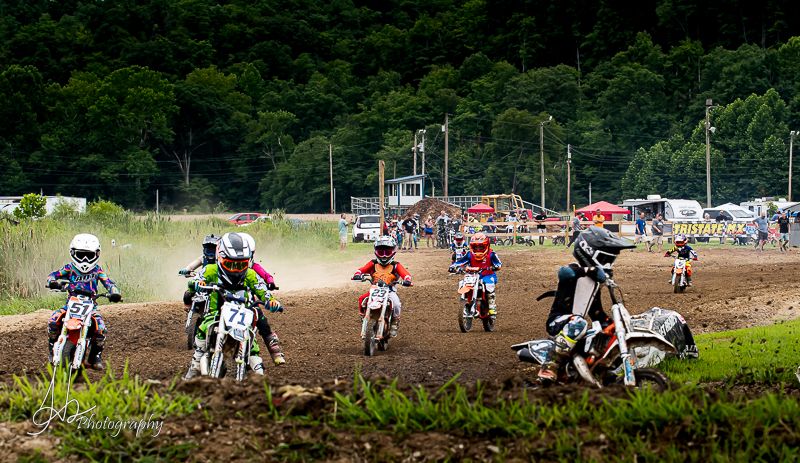 Panoramic view of motocross race with multiple riders on outdoor dirt track.