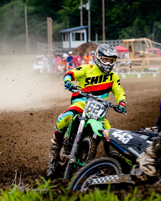 Motocross rider in neon yellow jersey races through dirt track on green motorcycle.