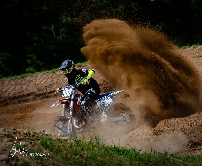 Dirt bike rider kicking up dust while cornering on outdoor motocross track.