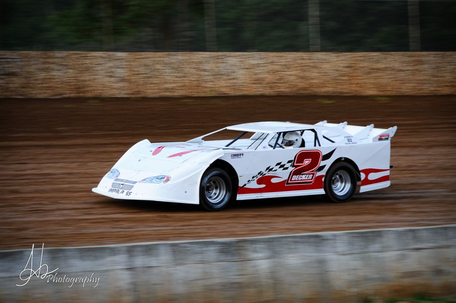 White late model stock car racing on dirt oval track during competition.