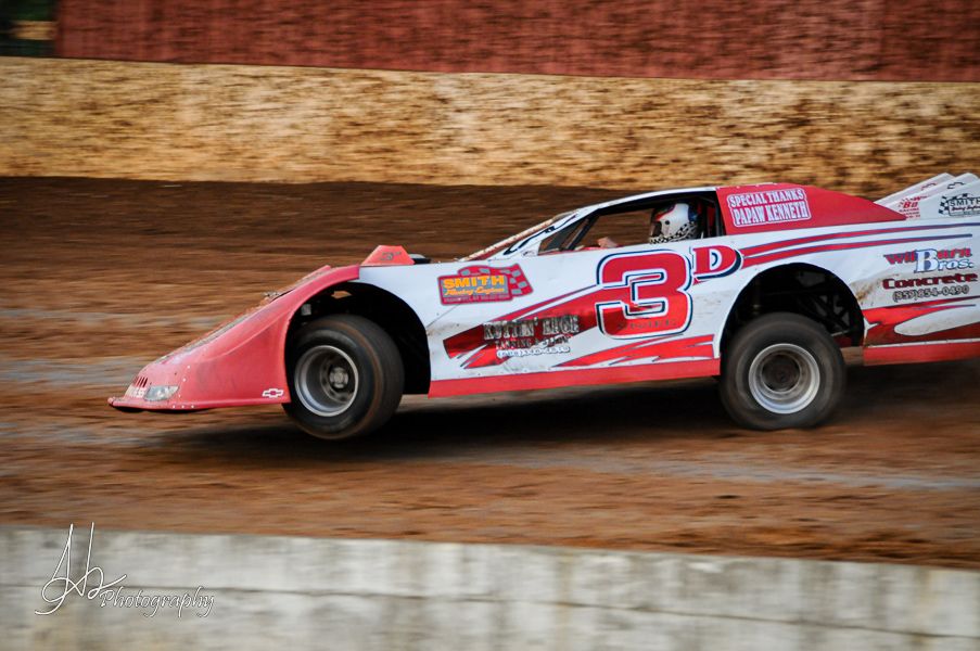 Racing cars compete on a dirt track during an intense motorsport competition.