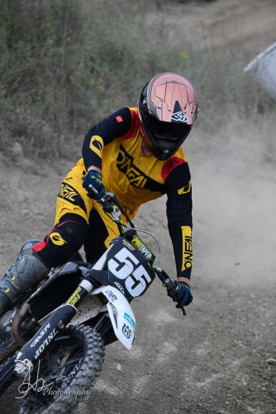 Rider in yellow jersey navigates dirt track on white motocross bike.