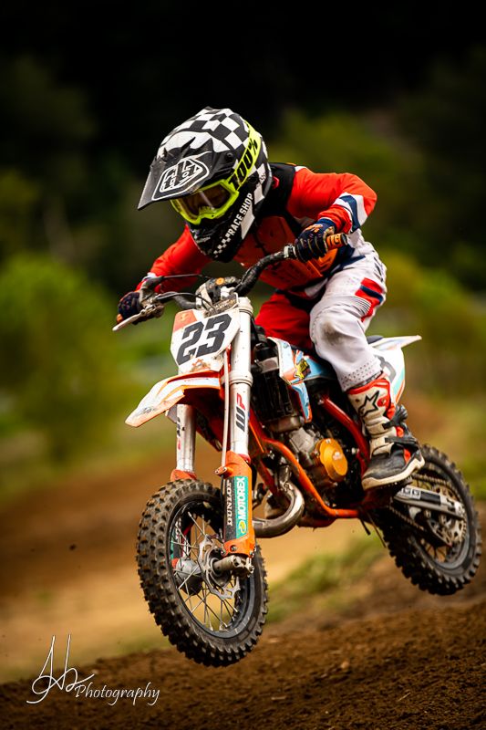 Red motocross bike performing dynamic jump on dirt track during race.