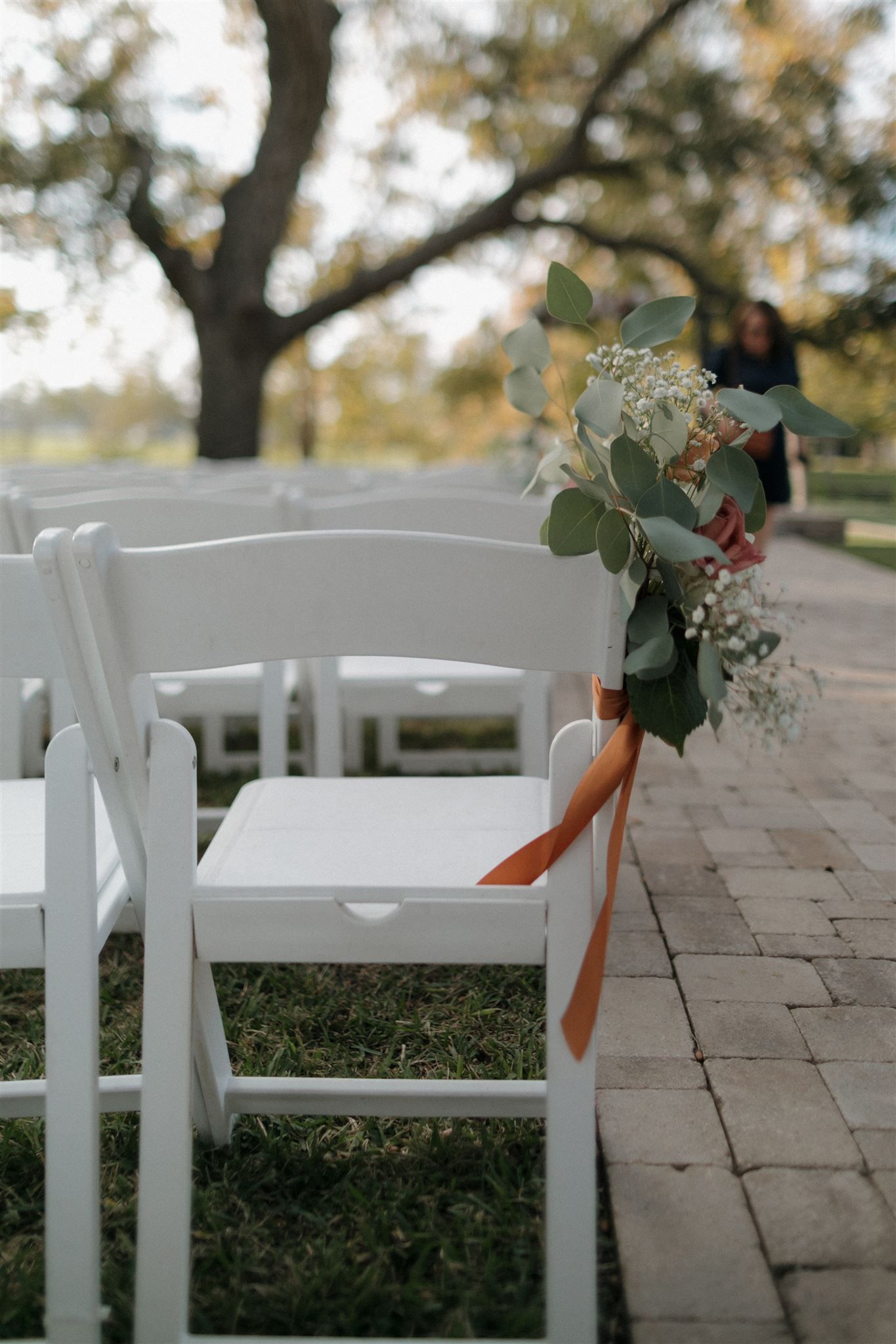 White folding chair decorated with eucalyptus and peach ribbon for outdoor wedding ceremony.