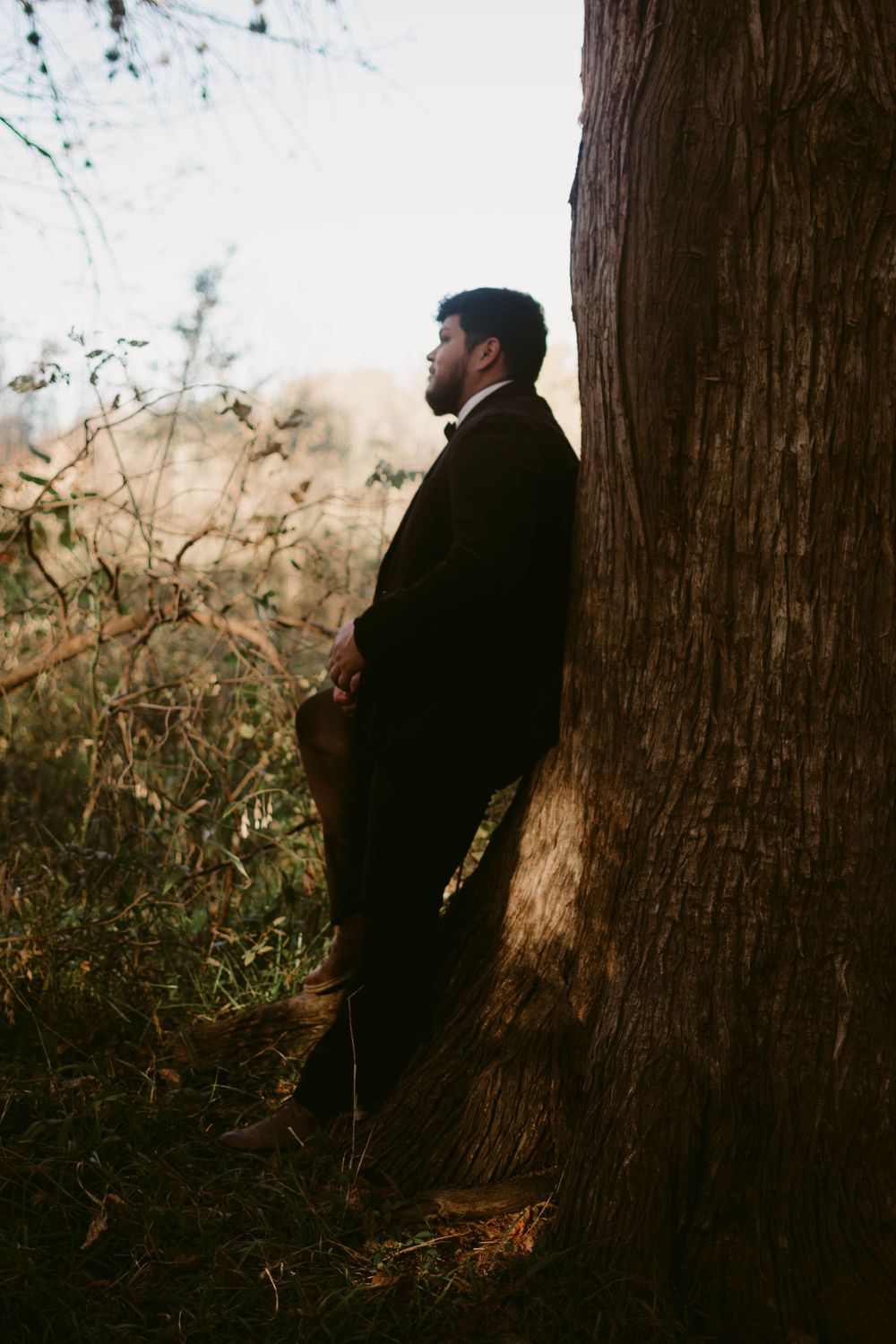Dramatic silhouette portrait against a tree trunk in formal attire.