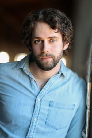 Professional headshot of a person with beard wearing light blue denim shirt.