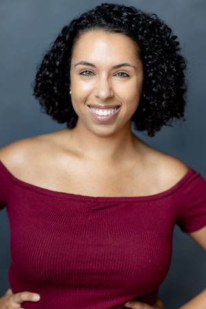 Professional headshot featuring a woman in a burgundy top with natural curly hair.