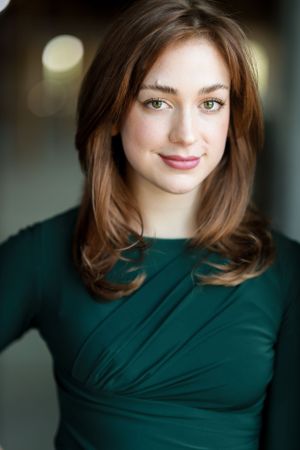 Professional headshot of someone in a dark green top with warm lighting and soft brown hair.