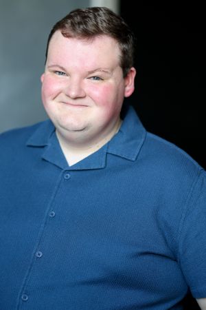 Professional headshot of a person in blue polo shirt against dark background.