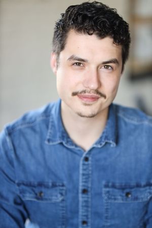 Professional headshot featuring someone in a denim shirt against a light background.