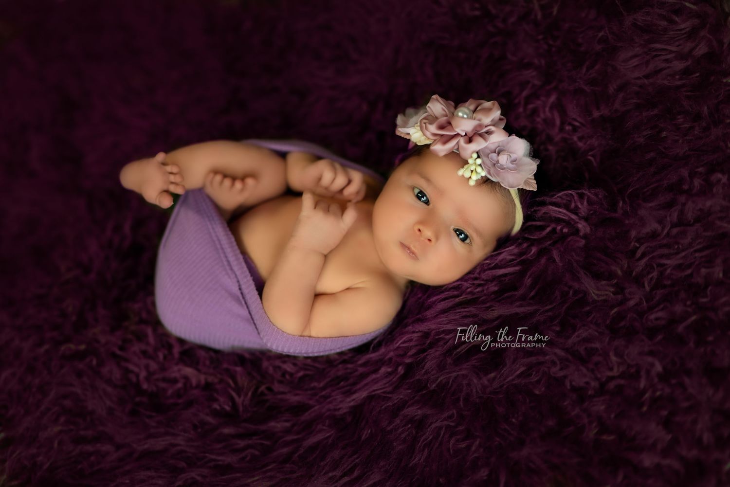 Newborn baby sleeping peacefully on dark textured background wearing delicate accessories.