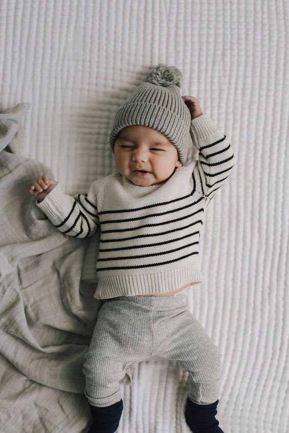 Baby in striped sweater and gray knit beanie lying on textured white blanket.