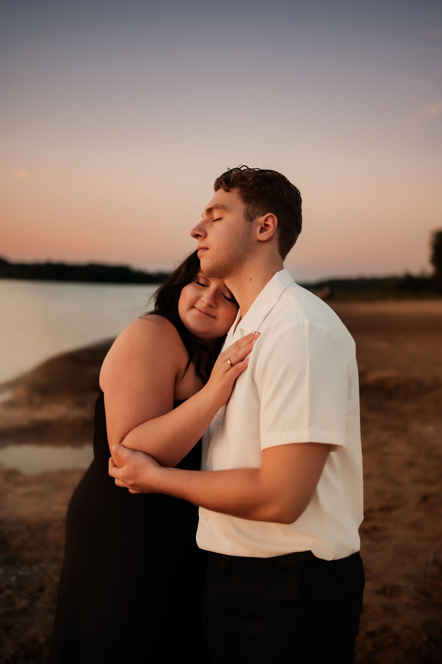 Romantic couple embraces on beach at sunset creating intimate silhouette against peaceful water.