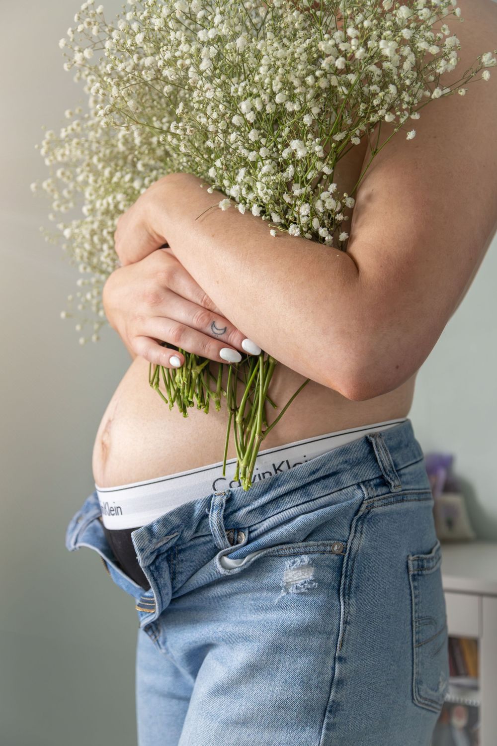 Person holding delicate baby's breath flowers against torso wearing distressed denim jeans.