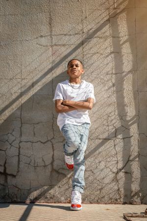 Urban portrait against textured wall with dramatic shadow patterns and natural lighting.