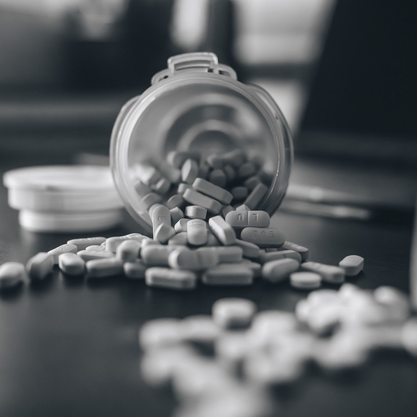 Prescription pills spilling out of bottle in black and white close-up photograph.