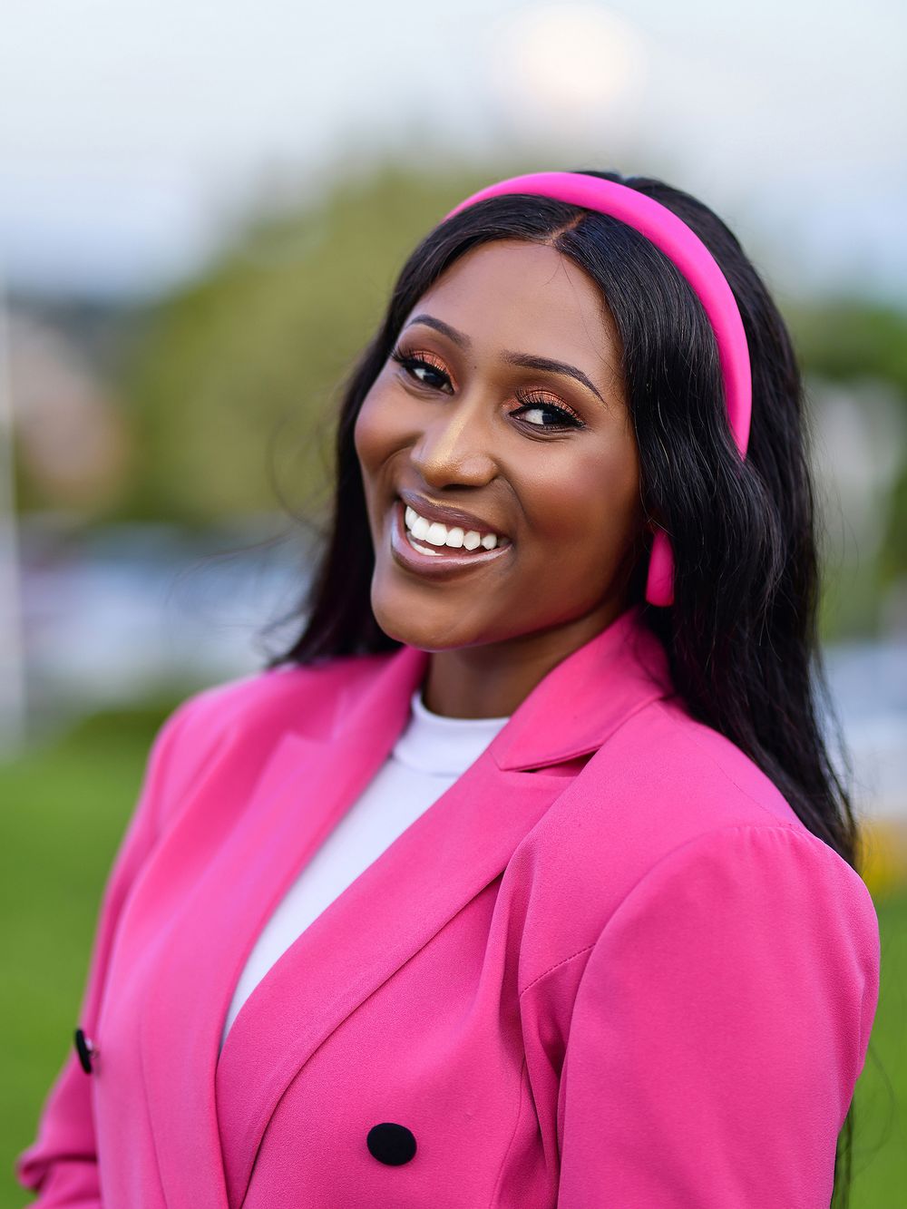 Professional wearing bright pink blazer and headband against outdoor background.