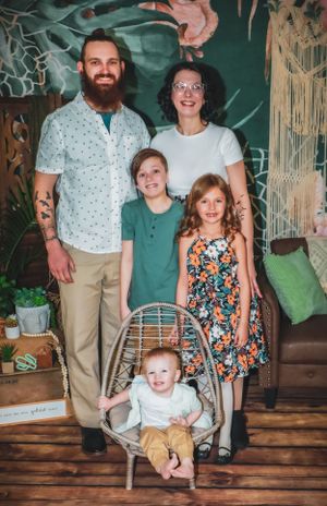 Family members pose together in coordinated outfits against a tropical-themed studio backdrop.