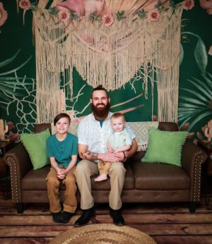 A family seated on a brown leather couch against a macrame wall hanging and green backdrop.