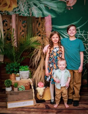 Tropical themed photo setup with green backdrop, palm leaves and rustic decor elements.