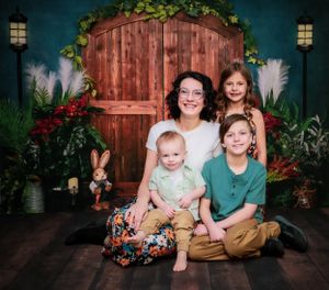 A casual portrait session in front of a rustic wooden wall with decorative greenery.