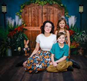 A family photo session in a cozy studio setting with wooden backdrop and floral decorations.