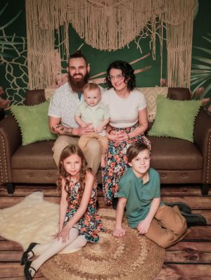 Family photo session on brown leather couch with tropical themed backdrop and decor.