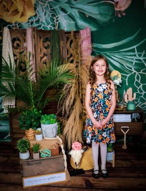 Tropical themed photo session with green backdrop, macrame wall hanging and palm leaves.