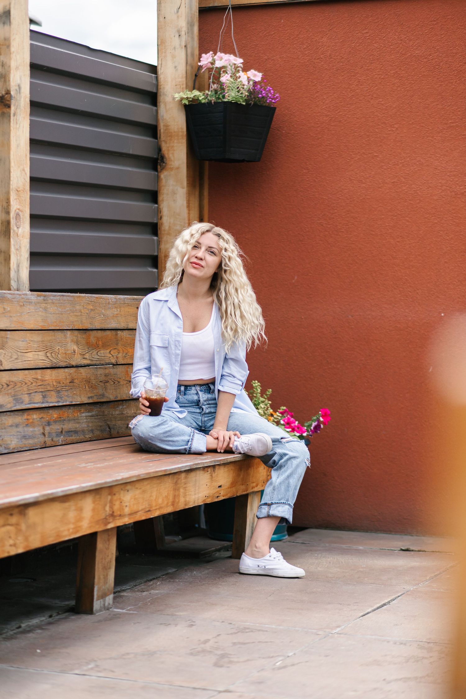Person in casual denim outfit sitting on wooden bench against terracotta wall.
