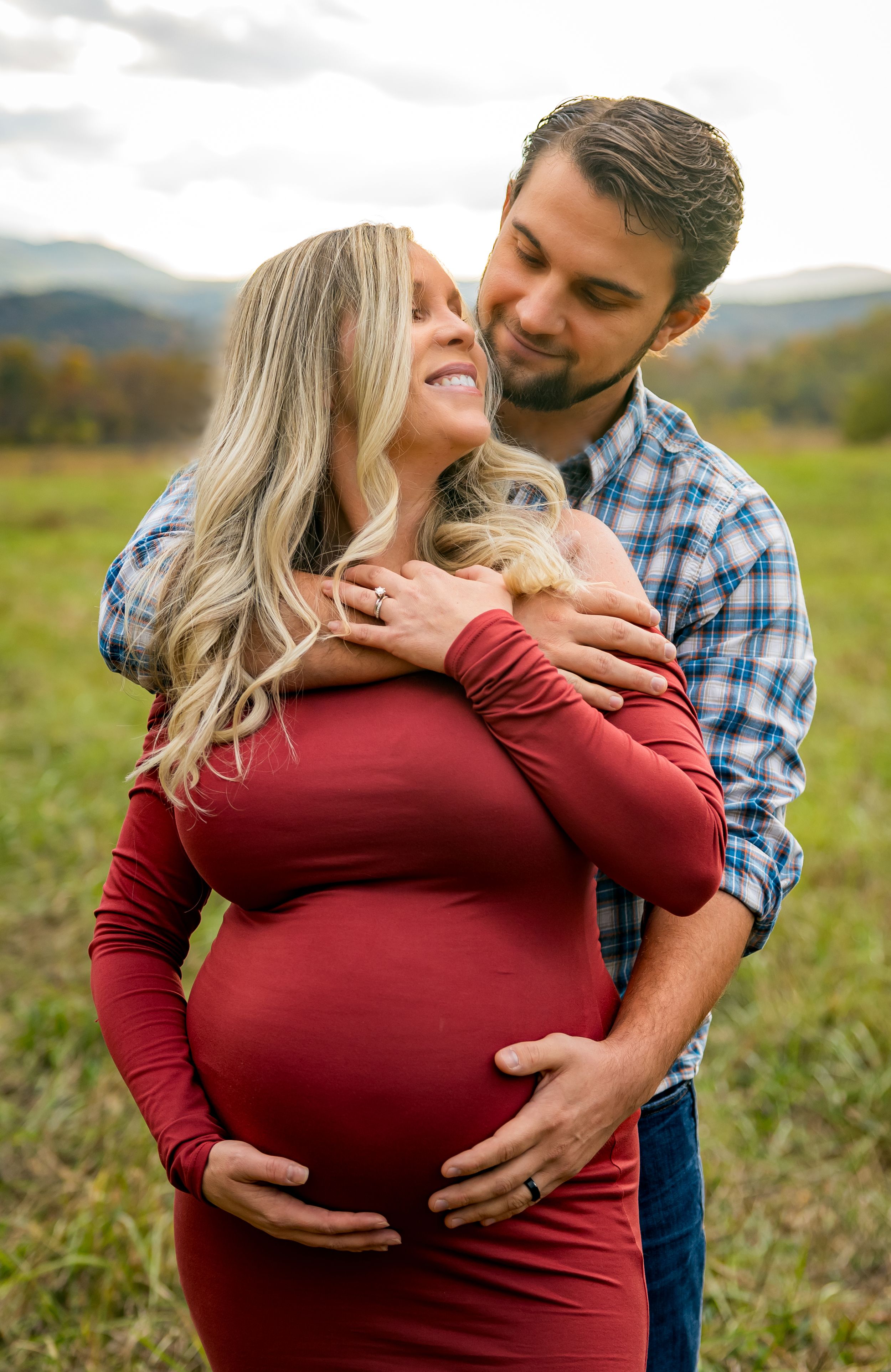 Maternity photo of couple embracing in a scenic mountain field during autumn.
