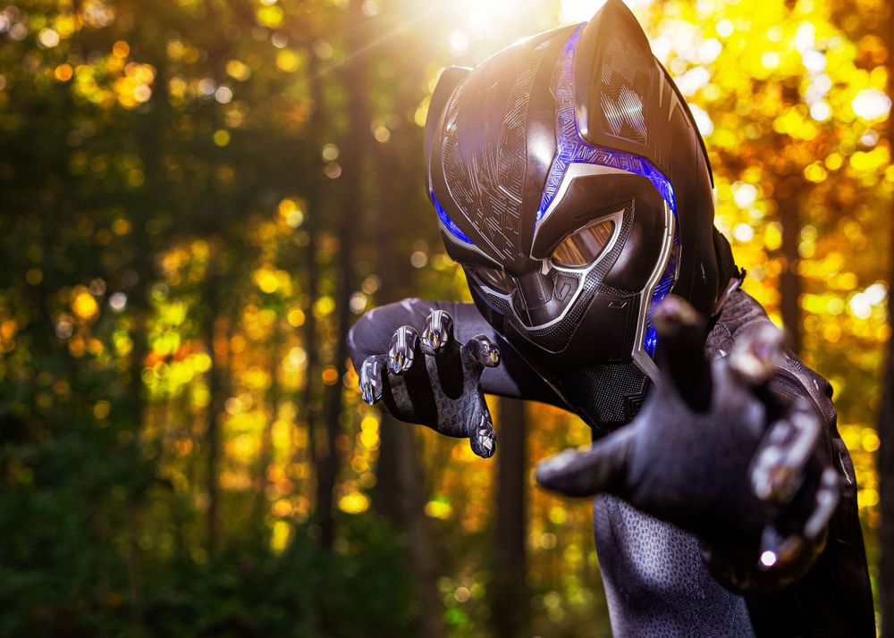 Black Panther cosplayer in full costume and glowing mask poses dramatically in a sunlit forest.