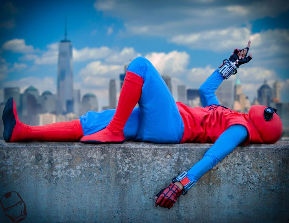 Spider-Man cosplayer in classic red and blue suit relaxes on rooftop with NYC skyline.