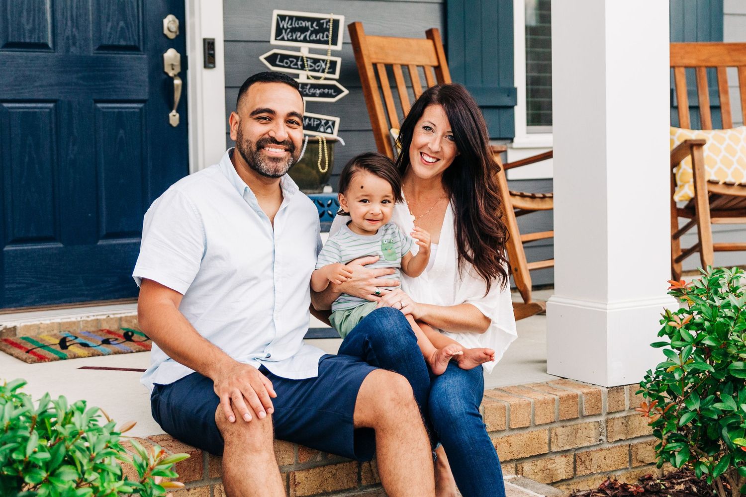 A family of three smiles on their front porch