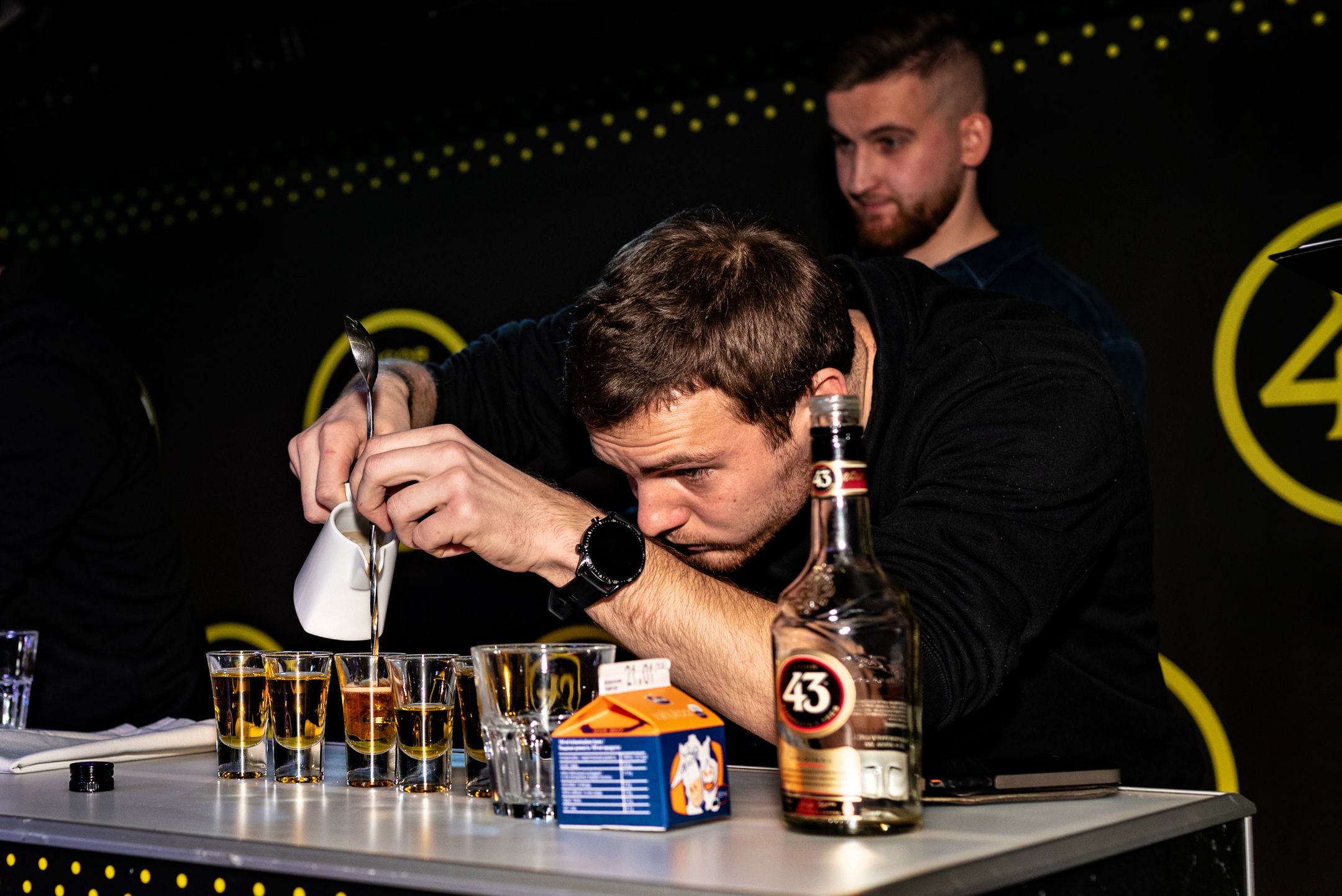 Concentrated bartender carefully measuring and pouring ingredients for cocktails at a Licor 43 event.