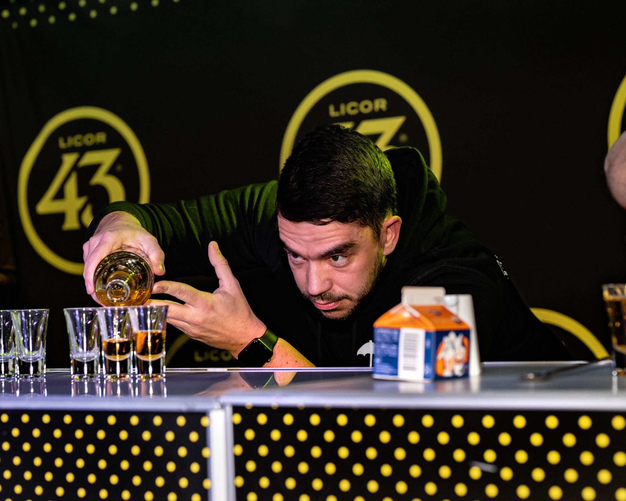 Bartender precisely pouring liquid into shot glasses at a Licor 43 branded bar.