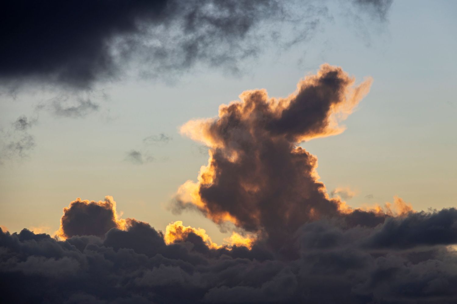 A single sunlit cloud towers above the horizon, glowing gold against a darkening sky.