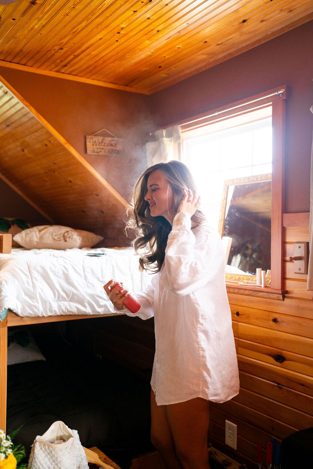 A bright morning light streams through a window in a cozy cabin bedroom with wood paneling.