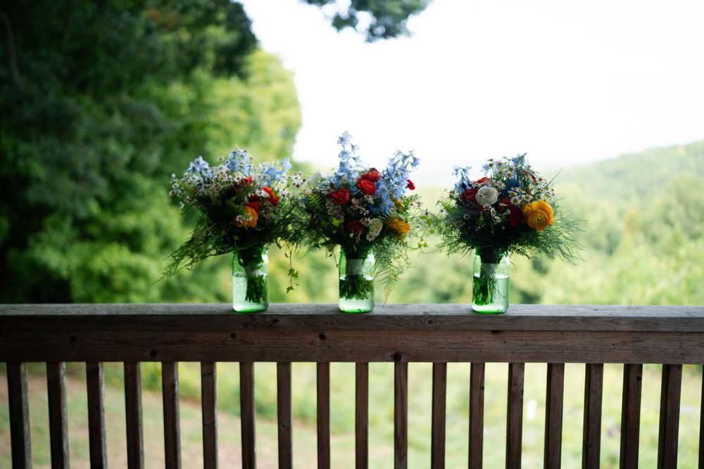 Three matching floral arrangements in green vases displayed on outdoor deck railing.