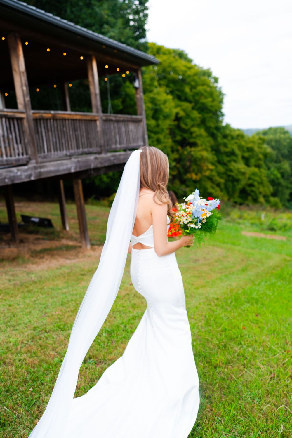 A wedding dress with a long flowing veil against the backdrop of a rustic wooden pavilion.