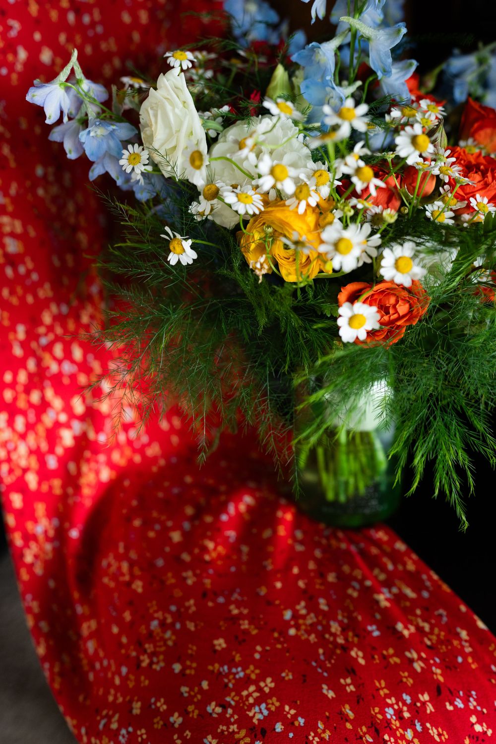 Wildflower bouquet with daisies and delphinium against red patterned fabric.